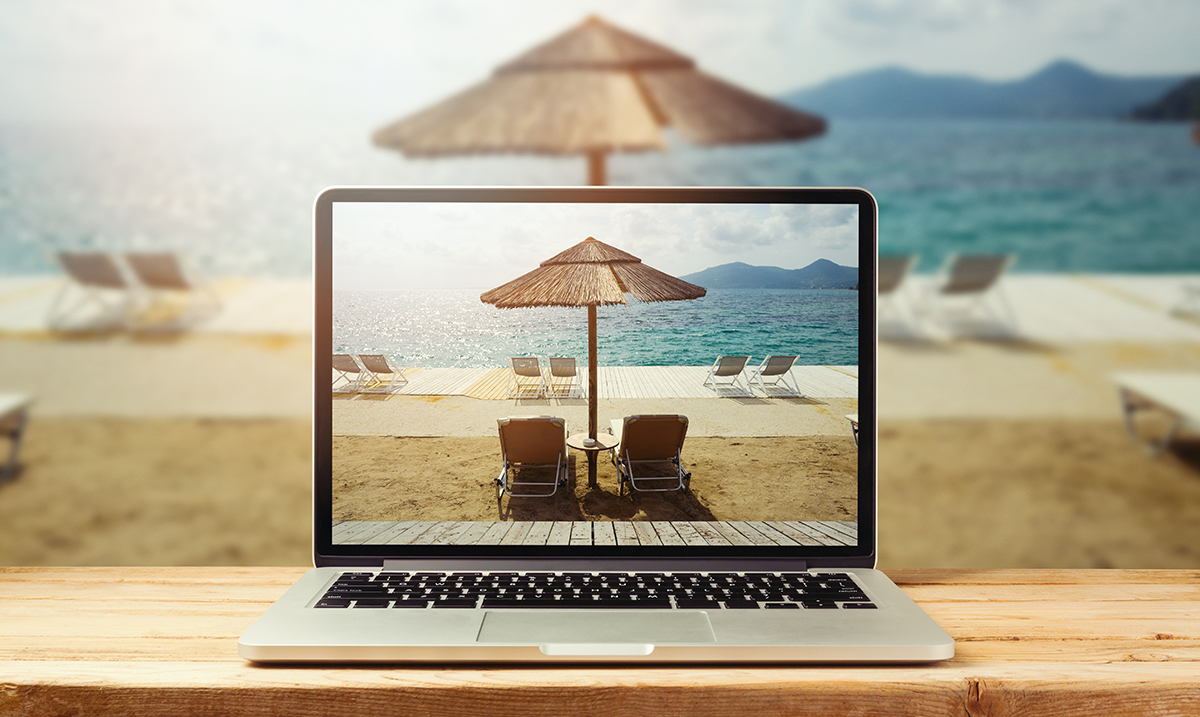 Laptop computer with sunny beach image on wooden table. Summer v